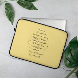May include: A yellow laptop sleeve with a black border. The sleeve features a quote from 2 Corinthians 3:18 in black script, surrounded by gold star accents. A laptop is partially visible.