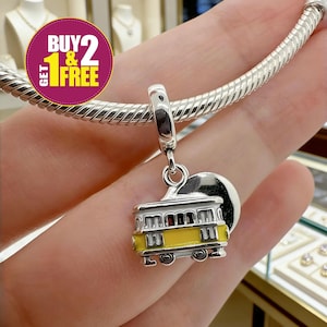 May include: A silver charm with a yellow and white trolley design. The charm is attached to a silver bracelet. The image also includes a purple and yellow circular graphic with the text "BUY 2 GET 1 FREE".