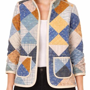 May include: A quilted jacket with a patchwork design in shades of blue, yellow, and brown. The jacket has a cream-colored trim, two front pockets, and a stand-up collar. The sleeves are three-quarter length.