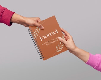 May include: A spiral-bound journal with a terracotta cover is being passed between two hands. The cover features the word "Journal" in white, along with the text "A Guide to Self Discovery" and decorative leaf accents.