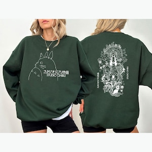 May include: Dark green sweatshirt with a white outline of a cartoon character and Japanese text on the front. The back features a detailed white illustration of characters and Japanese text. The sweatshirt has a crew neck design.