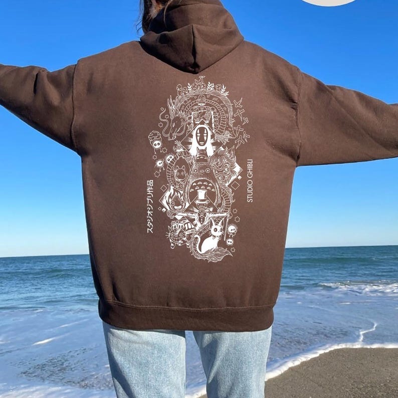 May include: A brown hoodie with a white graphic print on the back, depicting characters and text from Studio Ghibli films. The hoodie has a hood and long sleeves. The text "スタジオジブリ作品" and "STUDIO GHIBLI" are visible.