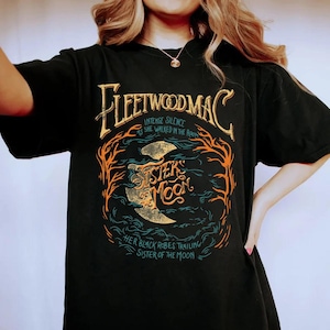 May include: Black t-shirt with the band name "Fleetwood Mac" in gold lettering. The shirt features the text "Intense Silence As She Walked In The Room" and "Sister of the Moon" with a crescent moon graphic in a circular design.