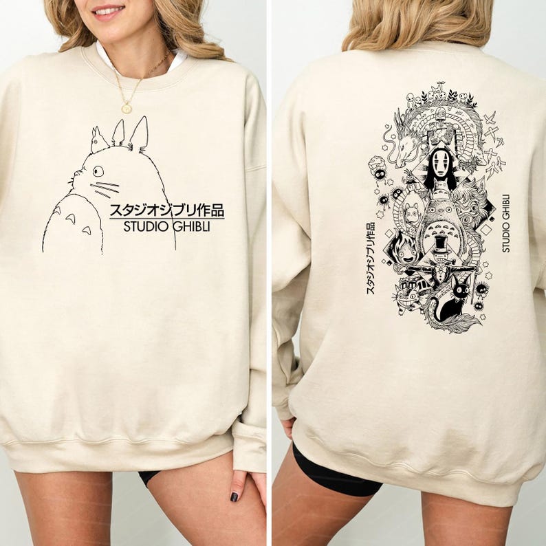 May include: Beige sweatshirt with a black and white Studio Ghibli character illustration on the front. The text "スタジオジブリ作品 STUDIO GHIBLI" is printed below the character. The back of the sweatshirt features a larger illustration of various Studio Ghibli characters.