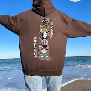May include: A brown hoodie featuring a stacked graphic of Studio Ghibli characters, with Japanese text on the left and "STUDIO GHIBLI" on the right. The design includes characters like Totoro and No-Face.