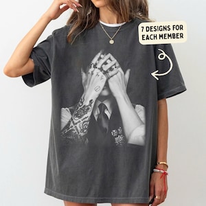 Könnte beinhalten: Dunkelgraues T-Shirt mit einem Schwarz-Weiß-Bild einer Person mit Tätowierungen und Ringen, die ihr Gesicht bedecken. Der Text "7 DESIGNS FOR EACH MEMBER" befindet sich in einem gelben Rechteck oben rechts.