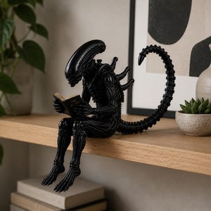 Op de afbeelding: Een zwart beeldje van een Xenomorph-wezen dat op een richel zit en een klein open boek leest. Het wezen heeft een gladde, langwerpige kop, gesegmenteerde ledematen en een lange, gebogen staart die achter de rug omhoog krult.