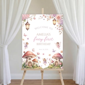 May include: A welcome sign for Amelia's first birthday, featuring a whimsical fairy theme. The sign includes illustrations of fairies, mushroom houses, flowers, and lanterns. The text reads "Welcome to Amelia's fairy first birthday" and the date May 24, 2026.