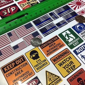May include: Sheet of stickers featuring American flags, blue line flags, and various warning signs. Includes signs that read "Keep Out," "Warning," and "Emergency Exit." A green ruler and two quarters are also visible.