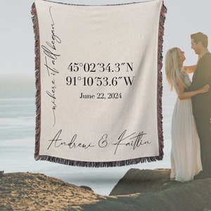 May include: A woven throw blanket with the text "where it all began" and coordinates 45°02′34.3″N 91°10′53.6″W. The text "June 22, 2024" and "Andrew & Kaitlin" are also printed on the blanket.