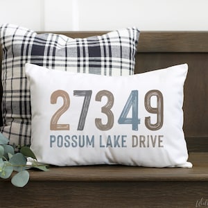 May include: A white cushion with the number 27349 and the text "Possum Lake Drive" in blue and brown lettering. The cushion is on a wooden bench with a black and white checked cushion behind it.