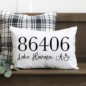 May include: White cushion with black text that reads "86406 Lake Havasu, AZ" on a wooden bench with a black and white checked cushion behind it.