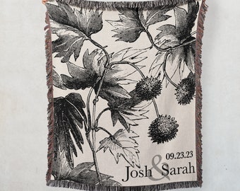 Könnte beinhalten: Eine gewebte Wolldecke mit einem botanischen Druck in Schwarzweiß. Die Decke hat einen Fransenrand und trägt den Text "09.23.23 Josh & Sarah".