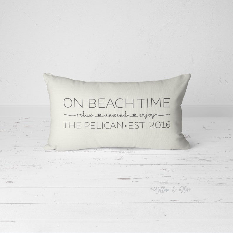 Puede incluir: Almohada rectangular blanca con texto negro que dice "On Beach Time relax unwind enjoy The Pelican Est. 2016".