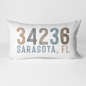 May include: White lumbar pillow with the text "34236 SARASOTA, FL" in a colorful, hand-painted style.