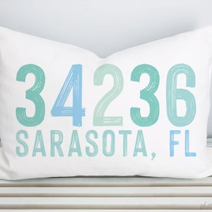 May include: White pillow with blue and green text that reads "34236 Sarasota, FL".