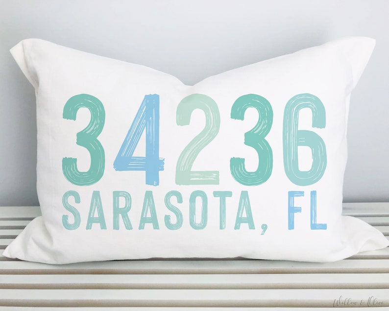 May include: White pillow with blue and green text that reads "34236 Sarasota, FL".
