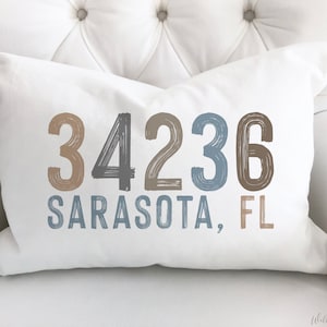 May include: White throw pillow with the text "34236 SARASOTA, FL" in a blue, gray, and brown color scheme.