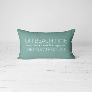 Puede incluir: Una almohada de tiro azul turquesa con texto blanco que dice "On Beach Time relax unwind enjoy The Pelican Est. 2016".