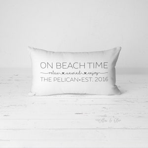 Puede incluir: Almohada rectangular blanca con texto negro que dice "On Beach Time relax unwind enjoy The Pelican Est. 2016".