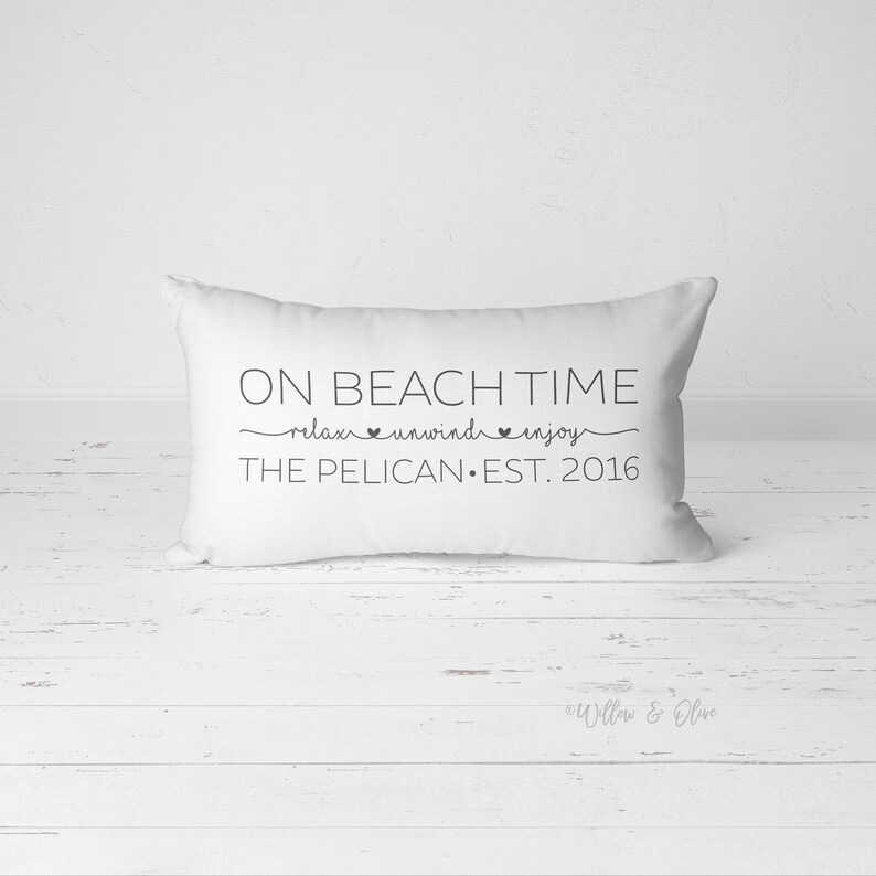 Puede incluir: Almohada rectangular blanca con texto negro que dice "On Beach Time relax unwind enjoy The Pelican Est. 2016".