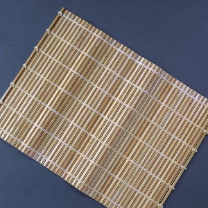 以下が含まれることがあります： 細い薄茶色の木製スラットを並べて作られた長方形の竹製マット。スラットは、マットの全幅にわたって一定の間隔で配置された細い白い水平方向の糸のステッチによってまとめられています。