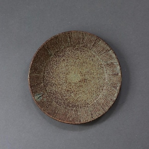 May include: A round ceramic plate featuring a speckled light green center and a dark brown rim. The rim is decorated with a series of fine, vertical etched lines that create a textured pattern around the entire circumference of the plate.