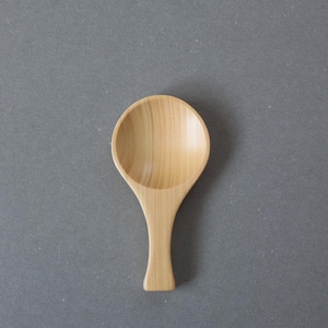 Pode incluir: Uma pequena colher de madeira com uma tigela arredondada e um cabo fino. A colher é feita de madeira clara e tem um acabamento liso e natural. A colher tem cerca de 15 cm de comprimento.