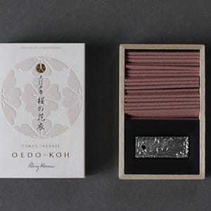 May include: A white box of Tokyo Incense Oedo-Koh Cherry Blossoms with a floral design and Japanese text next to an open wooden box containing incense sticks and a silver-colored metal piece.