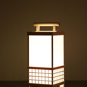 May include: A rectangular wooden lantern with a bright white light emanating from within. The lantern features a grid-like design on the lower section and a handle on top. The overall design is reminiscent of Japanese aesthetics.