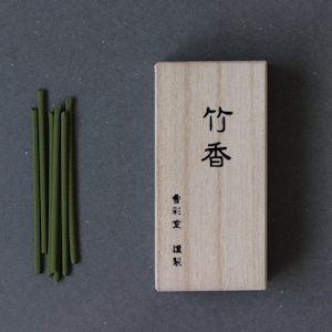 以下が含まれることがあります： 木製の箱と緑色の線香の束。箱には日本語の文字が黒インクで書かれています。線香は濃い緑色で、小さな束にまとめられています。