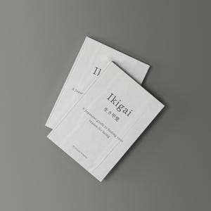 以下が含まれることがあります： 「Ikigai」というタイトルが黒字で書かれた2冊の白い本。本は灰色の背景にあります。本の表紙には日本語の文字と「生きがいを見つけるための日本のガイド」というテキストが書かれています。