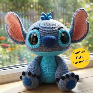 Op de afbeelding: Een handgemaakt gehaakt knuffel in de vorm van een blauw alien-personage met grote oren, grote ogen en een donkerblauwe neus. Het speelgoed is voornamelijk blauw en grijs, met roze accenten op de oren. De tekst "Bonus Gift Included" staat op een gele cirkel.