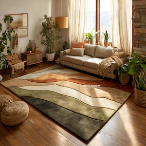 以下が含まれることがあります： 茶色、ベージュ、緑の色合いで山脈のデザインが施された大きな長方形のラグ。ベージュのソファ、植物、木の床があるリビングルームに配置されています。ラグのデザインは、部屋に自然でアースカラーの要素を追加します。