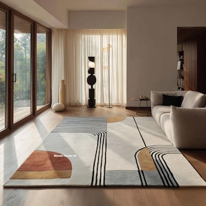 May include: A modern area rug with a geometric design. The rug features a combination of white, gray, rust, and black colors. The design includes curved and straight lines, creating a contemporary aesthetic. The rug is placed in a living room setting.