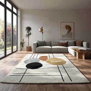 Könnte beinhalten: Ein cremefarbener Teppich mit geometrischem Design, das schwarze Linien und farbige Kreise in Grau, Braun, Schwarz und Gold aufweist. Der Teppich befindet sich in einem modernen Wohnzimmer mit grauem Sofa und großen Fenstern.