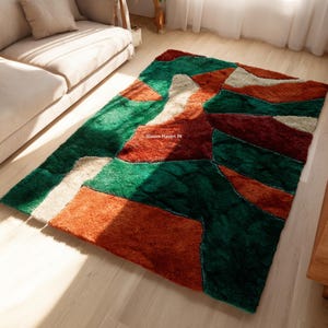 Può includere: Un tappeto rettangolare con un design geometrico. Il tappeto presenta un motivo patchwork nei toni del verde, arancione e crema. Il testo "Bloom Haven IN" è visibile sul tappeto. È posizionato su un pavimento in legno chiaro.