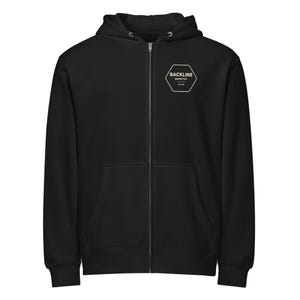 Puede incluir: Una sudadera negra con cremallera, capucha y bolsillos delanteros. La sudadera tiene un logotipo hexagonal blanco en el pecho con el texto "BACKLINE SUPPLY CO." y "EST 2019". La cremallera es plateada.