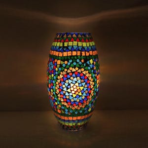 May include: An oval mosaic lamp with a vibrant design. The lamp is made up of small, colourful glass pieces in shapes like triangles and circles. The colours include blue, green, red, yellow, and orange. The lamp is lit from inside, creating a warm, inviting glow.