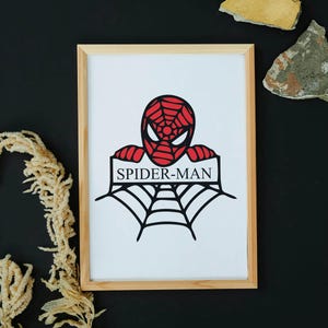May include: Framed artwork featuring a red and black Spider-Man design. The image shows Spider-Man's head and a web, with the text "SPIDER-MAN" below. The artwork is in a light wood frame, set against a black background.