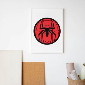 May include: Framed artwork featuring a black spider silhouette on a red webbed sphere. The artwork is displayed in a white frame against a white wall. The image evokes a comic book or superhero theme.