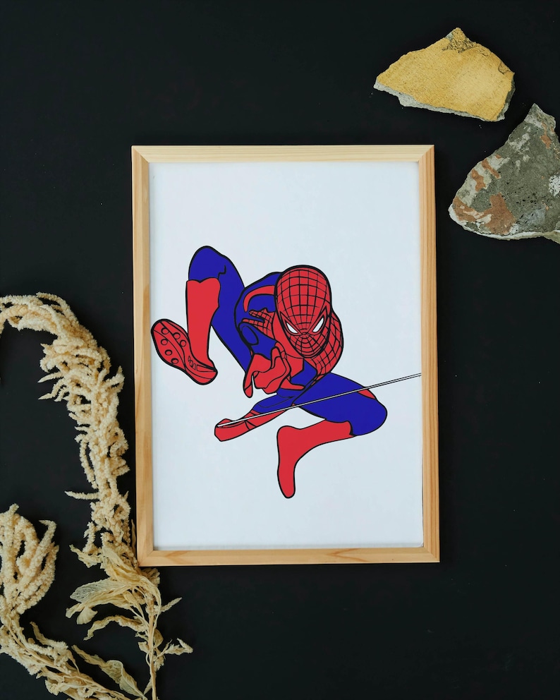 May include: Framed artwork featuring a stylized illustration of Spider-Man in a dynamic pose. The superhero is depicted in his classic red and blue costume, with a web extending from his hand. The artwork is set against a white background within a natural wood frame.