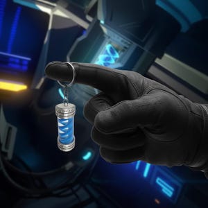 Puede incluir: Un llavero plateado con un colgante cilíndrico. El colgante tiene una carcasa exterior transparente con un diseño azul en forma de espiral en el interior. El llavero está sujeto por una mano enguantada sobre un fondo futurista iluminado en azul.