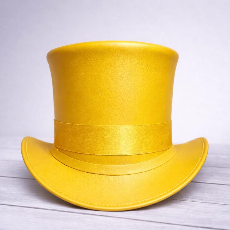 May include: A bright yellow top hat with a wide brim and a band around the crown. The hat is made of a smooth material and sits on a light-colored wooden surface. The hat's design is classic and elegant.