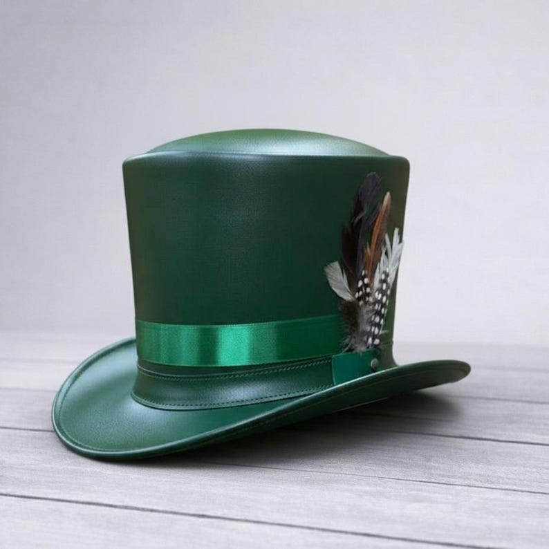 Puede incluir: Un sombrero de copa verde oscuro con una cinta a juego y un grupo de plumas. El sombrero tiene una corona alta y un ala ancha. Las plumas son marrones, negras y blancas.