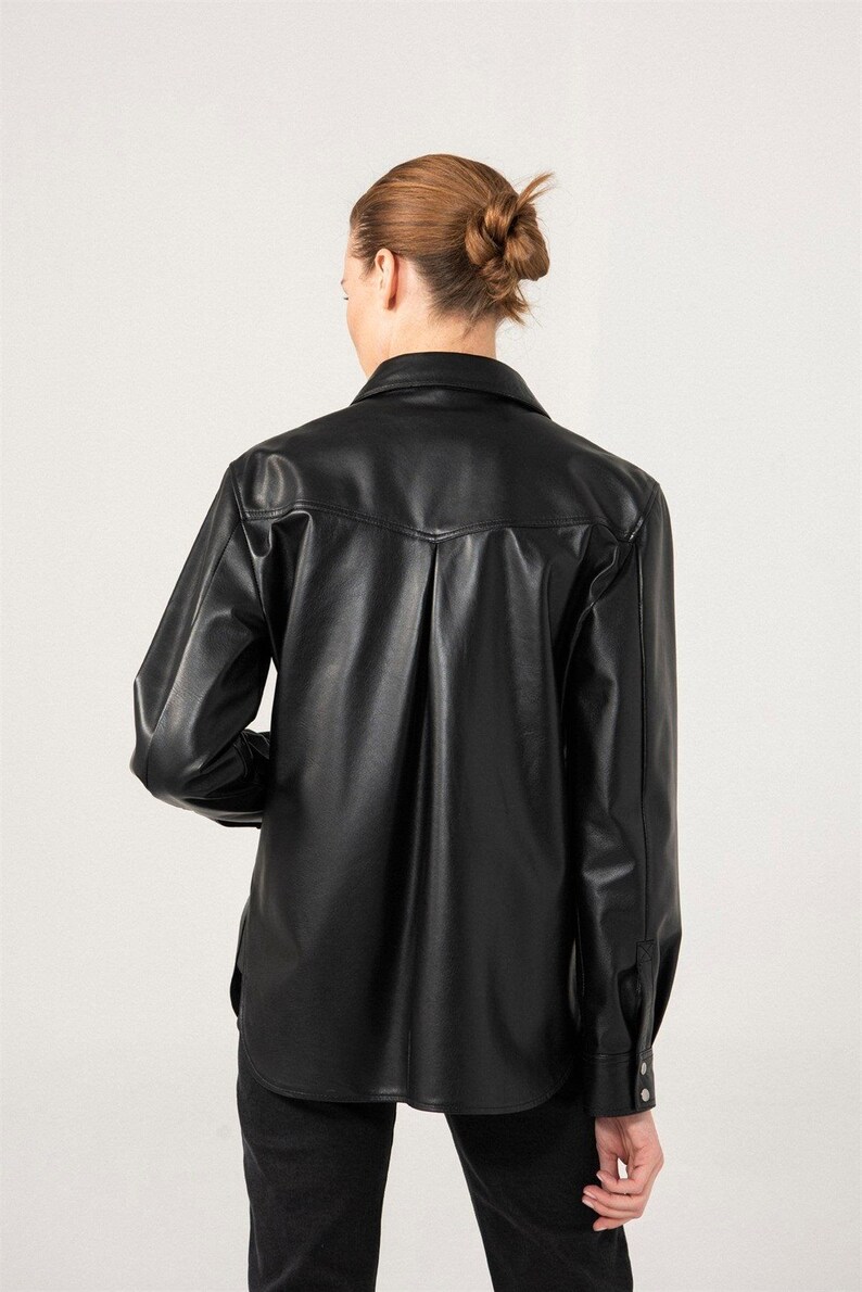 May include: Black long-sleeve button-down shirt made of faux leather. The shirt has a classic collar, buttoned cuffs, and a slightly oversized fit. The back features a vertical pleat detail.