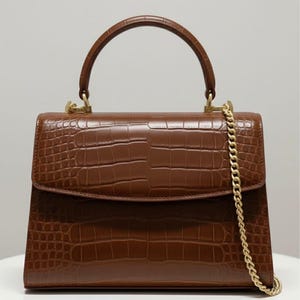 May include: A white ceramic mug with a black handle and the text "But First, Coffee" in a bold, black font. The mug is set against a blurred background, suggesting a cosy setting.