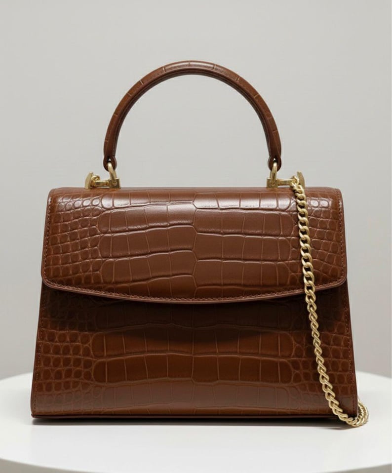 May include: A white ceramic mug with a black handle and the text "But First, Coffee" in a bold, black font. The mug is set against a blurred background, suggesting a cosy setting.