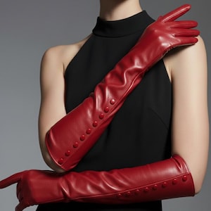 May include: Long, bright red leather gloves with button details. The gloves extend past the elbows and are a vibrant accessory. The gloves are a solid color and have a smooth texture. The buttons are evenly spaced along the length of the gloves.