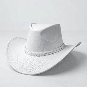 May include: A white cowboy hat with a textured, crocodile-like pattern. The hat features a braided band around the crown and a wide brim. The hat's dimensions are approximately 15 inches in length and 12 inches in width.
